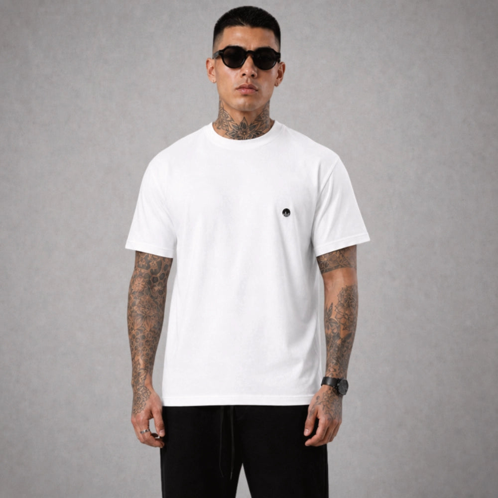 Ein weißes Boxy Cut T-Shirt der Marke FORCE ZERO im Rogue Mode Renegade Design zeigt als Ganzkörper-Modellbild die Vorderansicht an einem tätowierten Model mit Sonnenbrille, wobei auf der linken Brust ein kleiner, runder, schwarzer Logo-Print der Marke zu sehen ist.