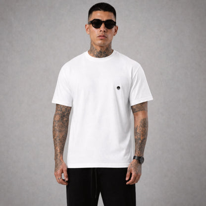 Ein weißes Boxy Cut T-Shirt der Marke FORCE ZERO im Rogue Mode Renegade Design zeigt als Ganzkörper-Modellbild die Vorderansicht an einem tätowierten Model mit Sonnenbrille, wobei auf der linken Brust ein kleiner, runder, schwarzer Logo-Print der Marke zu sehen ist.