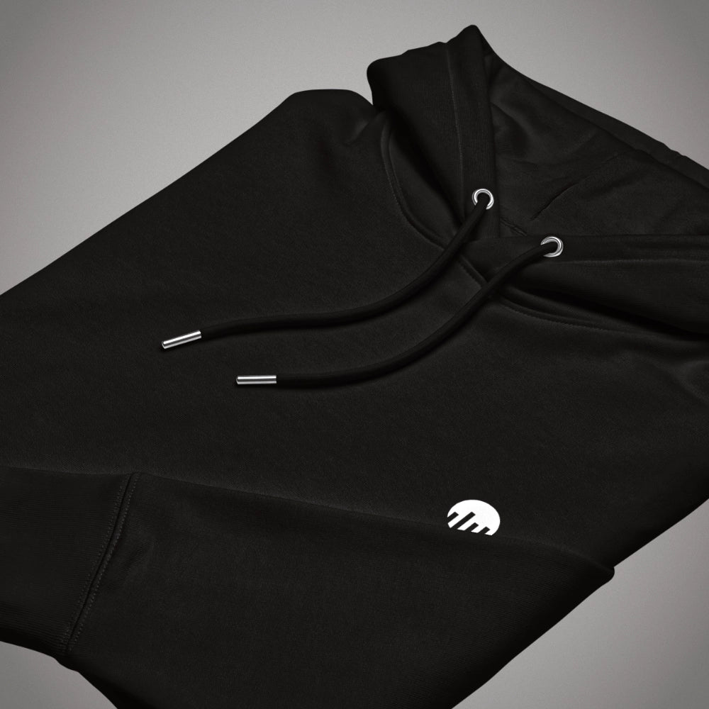 Ein schwarzer Core Fit Hoodie der Marke FORCE ZERO im Code Black Design zeigt als Produkt-Vorderansicht (Mockup) eine angewinkelte Ansicht des flach zusammengelegten Kapuzenpullovers mit Kordelzug, auf dem das runde FORCE ZERO Logo auf dem linken Ärmel in kontrastierendem Weiß gestickt oder gedruckt zu sehen ist.
