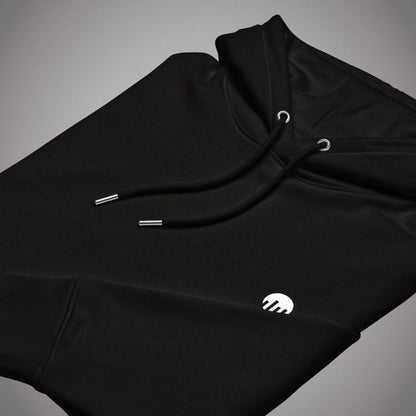 Ein schwarzer Core Fit Hoodie der Marke FORCE ZERO im Code Black Design zeigt als Produkt-Vorderansicht (Mockup) eine angewinkelte Ansicht des flach zusammengelegten Kapuzenpullovers mit Kordelzug, auf dem das runde FORCE ZERO Logo auf dem linken Ärmel in kontrastierendem Weiß gestickt oder gedruckt zu sehen ist.