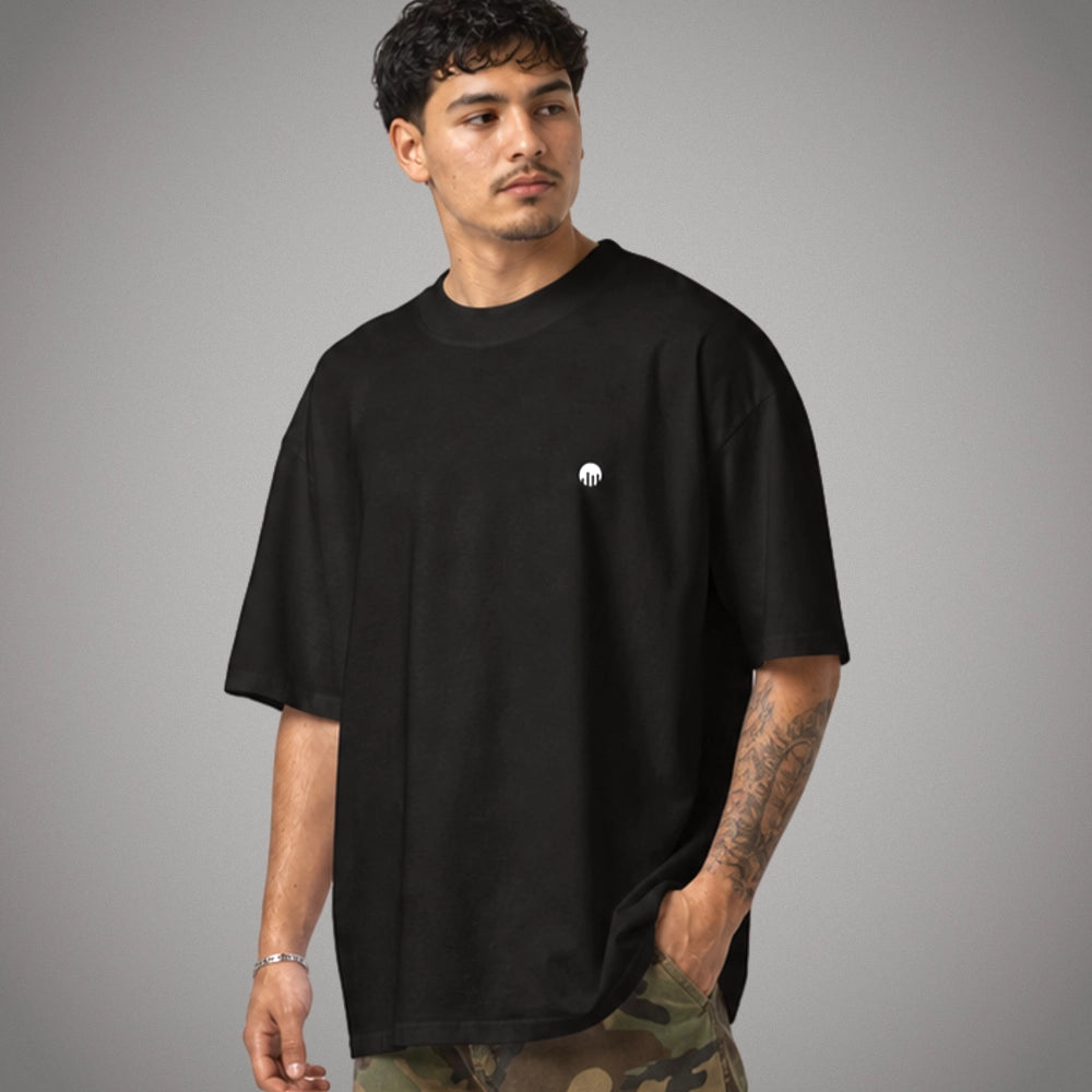 Ein schwarzes Oversized T-Shirt der Marke FORCE ZERO im Rogue Mode Raw Design am Model in einer halbseitig gedrehten Produkt-Vorderansicht mit einem kleinen, weißen Logo-Print auf der linken Brustseite.