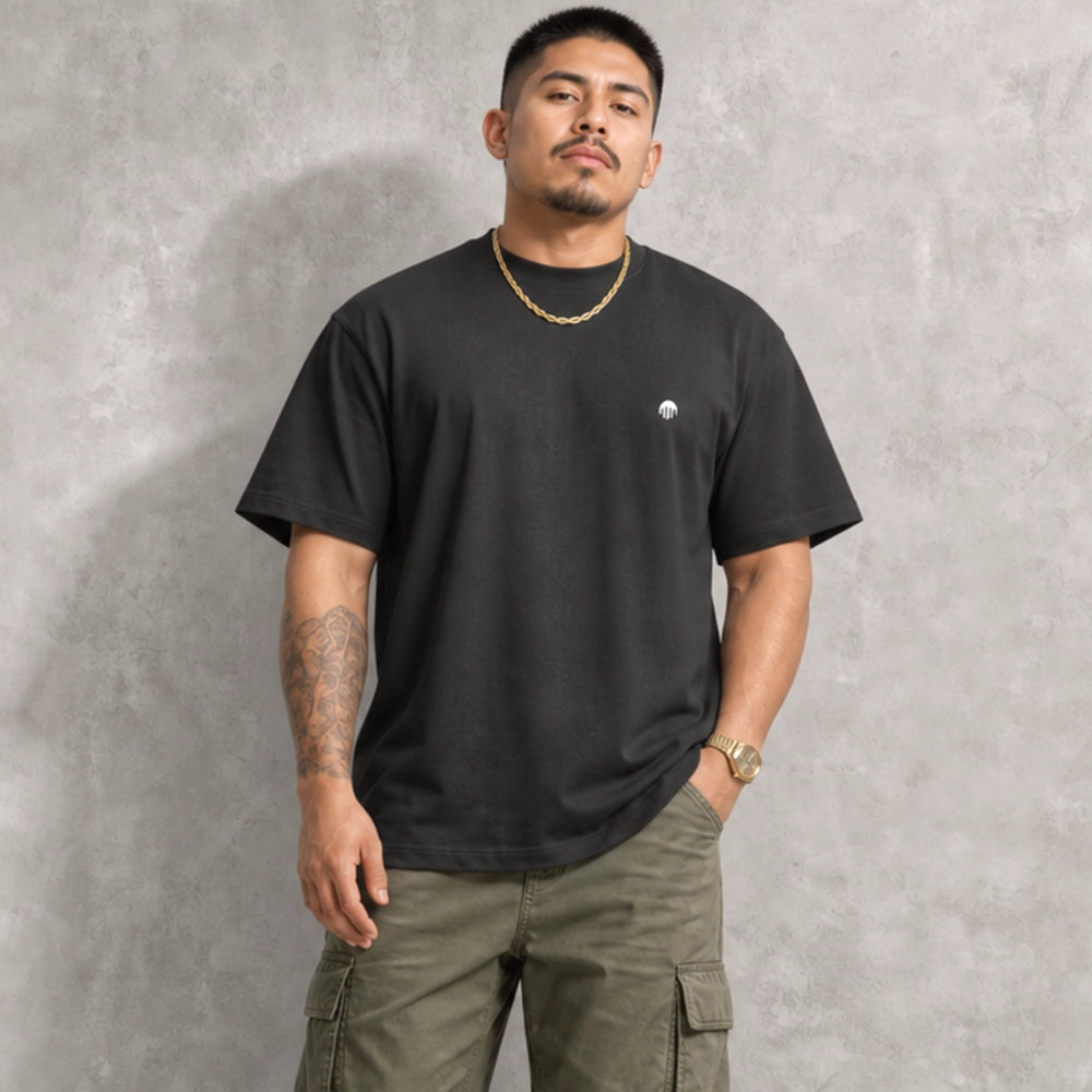 Ein schwarzes Boxy Cut T-Shirt der Marke FORCE ZERO im Rogue Mode Renegade Design zeigt als Ganzkörper-Modellbild die Vorderansicht an einem Model mit Halskette und Cargo-Hose, wobei auf der linken Brust ein kleiner, runder, weißer Logo-Print zu sehen ist.