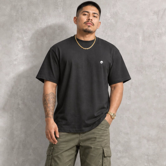 Ein schwarzes Boxy Cut T-Shirt der Marke FORCE ZERO im Rogue Mode Renegade Design zeigt als Ganzkörper-Modellbild die Vorderansicht an einem Model mit Halskette und Cargo-Hose, wobei auf der linken Brust ein kleiner, runder, weißer Logo-Print zu sehen ist.