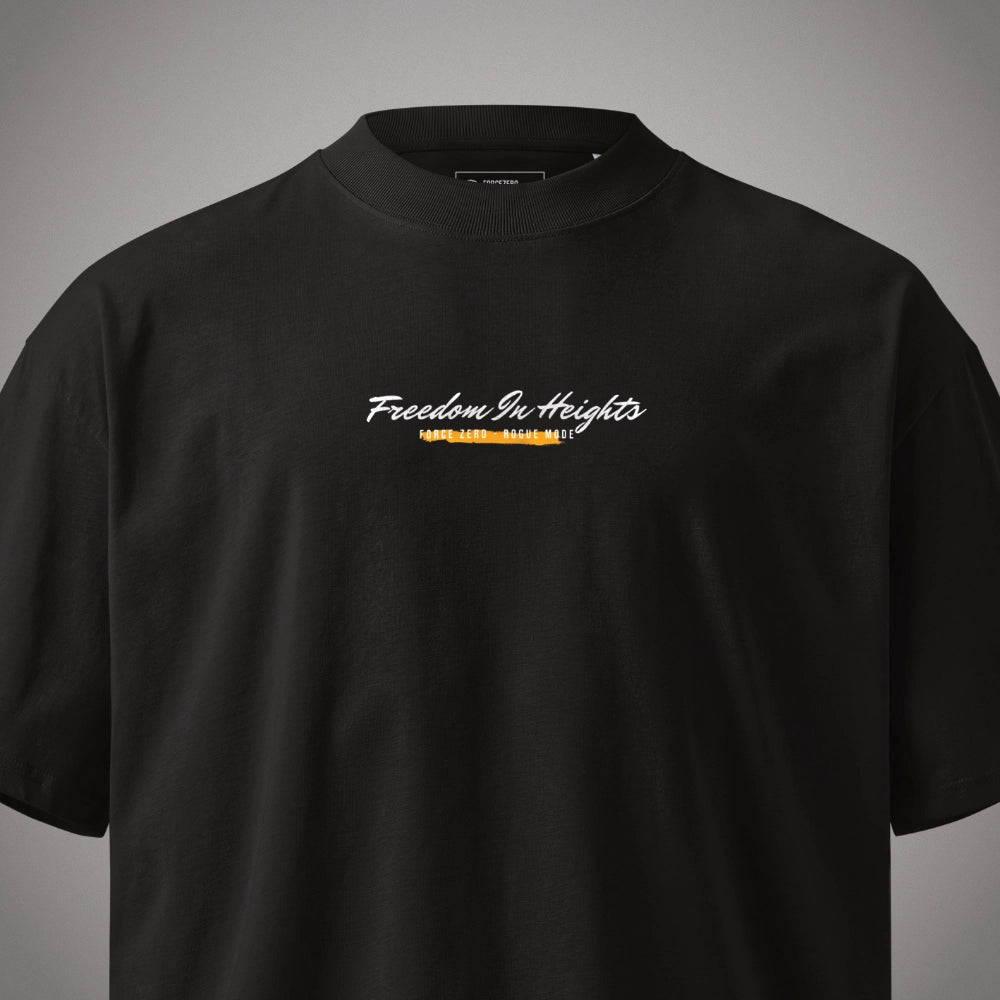 Eine Nahaufnahme von Kragen und Brustbereich eines schwarzen Oversized T-Shirts der Marke FORCE ZERO im Rogue Mode Rio X Design in der Produkt-Vorderansicht (Mockup) mit dem geschwungenen weißen Brustprint „Freedom In Heights“ über einer gelb-orangefarbenen, markierten Grafikelement-Unterzeilung.