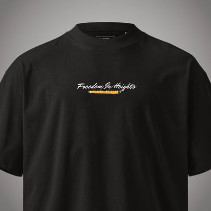 Eine Nahaufnahme von Kragen und Brustbereich eines schwarzen Oversized T-Shirts der Marke FORCE ZERO im Rogue Mode Rio X Design in der Produkt-Vorderansicht (Mockup) mit dem geschwungenen weißen Brustprint „Freedom In Heights“ über einer gelb-orangefarbenen, markierten Grafikelement-Unterzeilung.