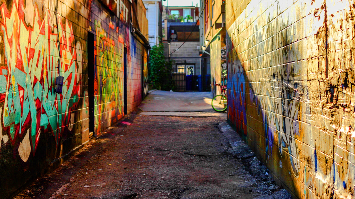 Ein farbenfrohes Ambiente Banner für die Rogue Mode Sektion zeigt eine schmale, urbane Gasse im Sonnenlicht, deren Backsteinwände großflächig mit bunten Graffiti-Schriftzügen und Streetart besprüht sind.